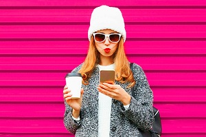 Young Woman Looking at Phone with Sunglasses and Coffee in hand